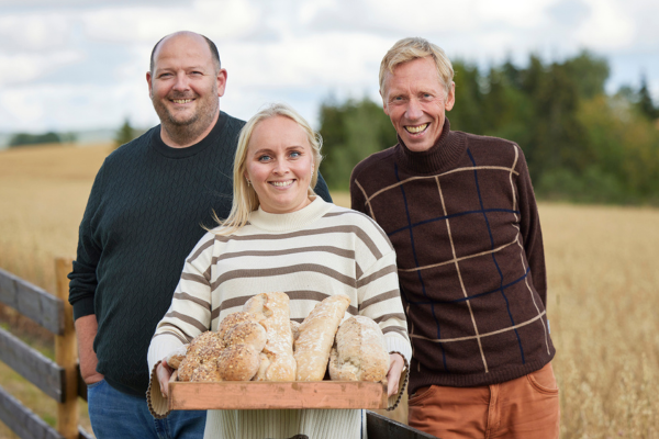Tre av våre distriktssjefer i kornåkeren med et brett med brød